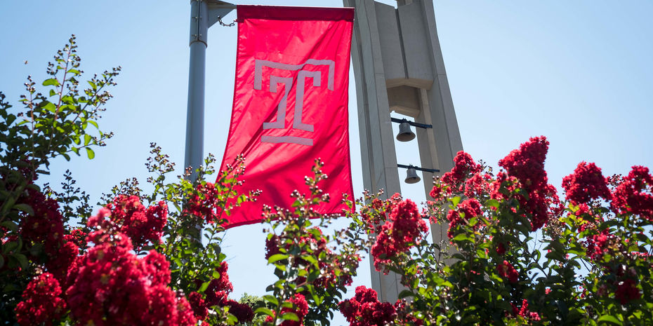 The cherry red Temple T flag waves in front of the bell tower on Polett Walk