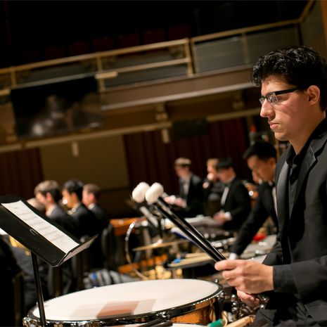 Student in a suit playing the drums at a concert