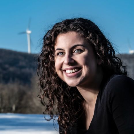 Andrea Poosikian smiles in front of three wind turbines standing in the distance.