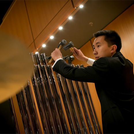 A student plays symphonic chimes as part of an orchestra performance.