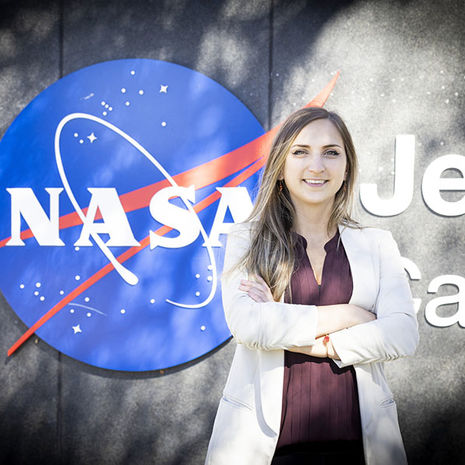 A woman stands in front of a NASA sign with her arms folded.