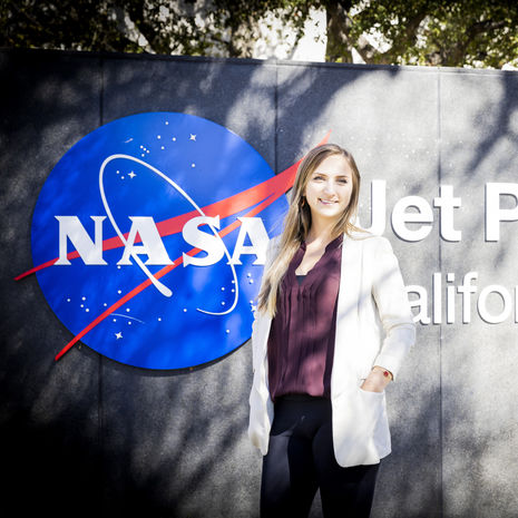 Shannon Hibbard smiling and wearing a white lab coat in front of NASA