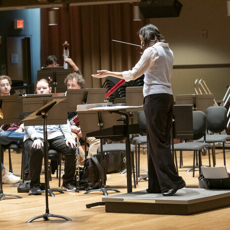Image of Matthew Levy soloing with the wind symphony. Patricia Cornett conducts while Emma O'Halloran observes.
