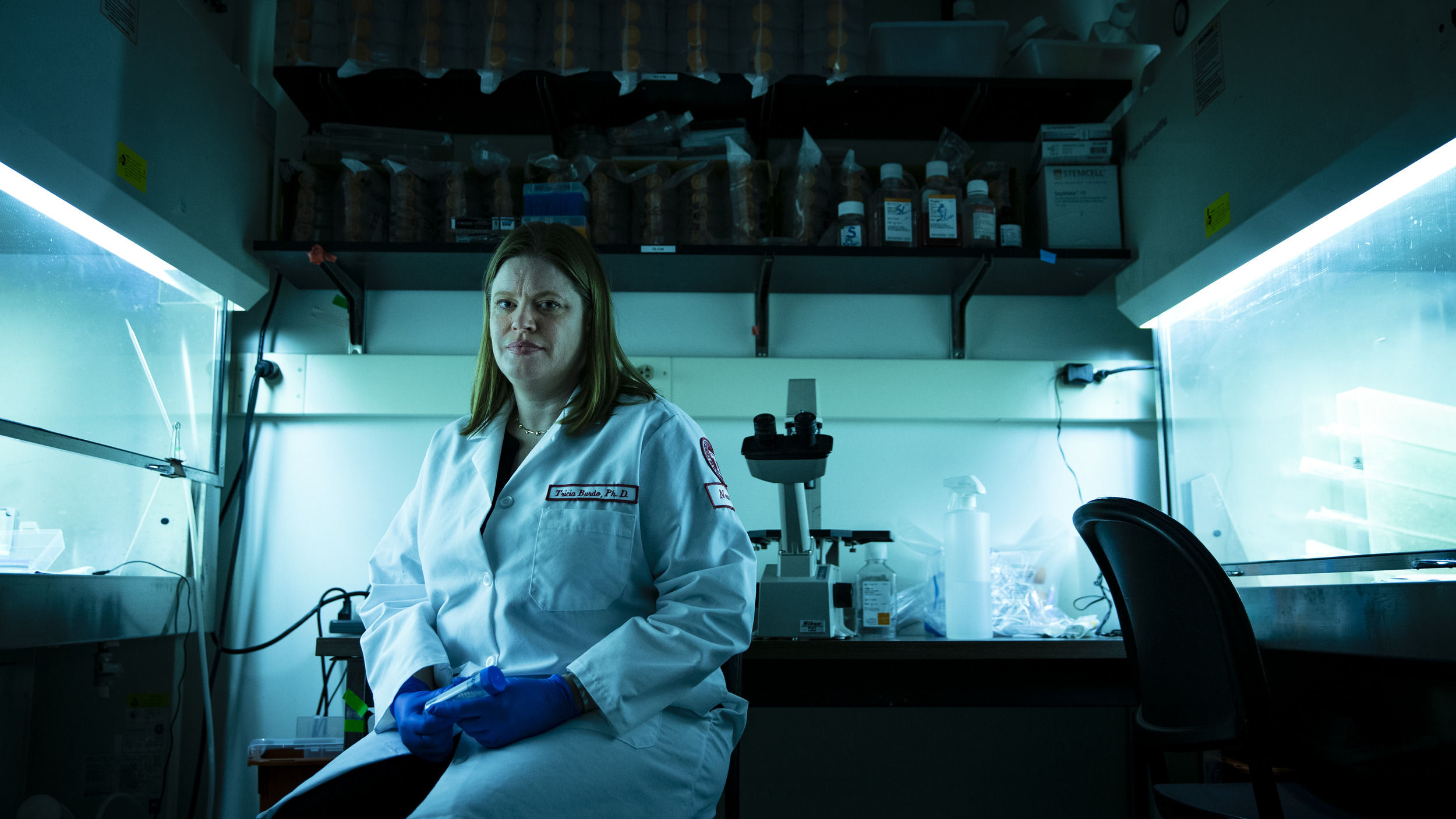 Tricia Burdo wearing a white lab coat and sitting the lab