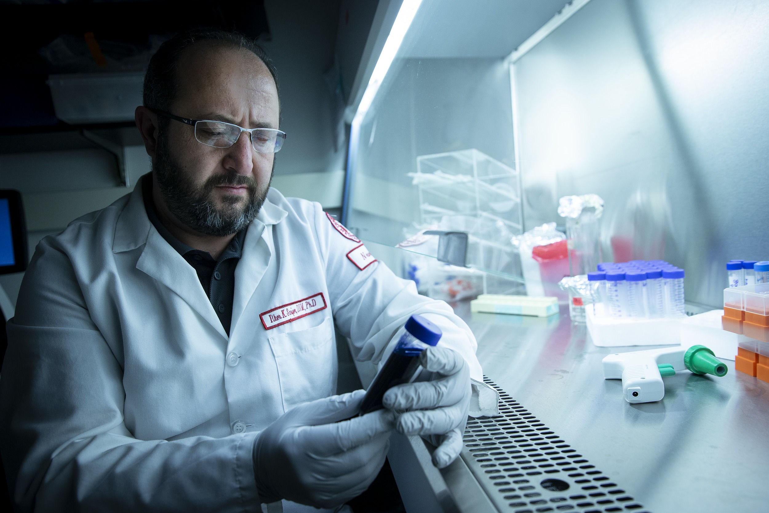 A man wearing a white lab coat and gloves holds a test tube