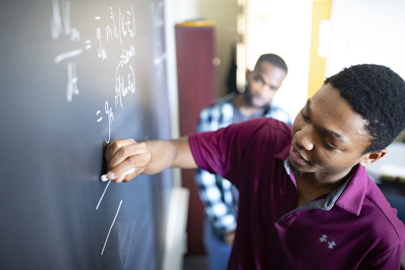 An image of a student writing a math equation on a chalkboard.