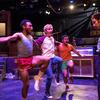Three guys dance and sing on stage with another actor looking on.
