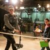 A student in a film studio carefully handles a camera while another student looks on.