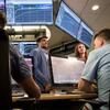 A group of business students analyze financial information, displayed on large screens.