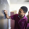 student and professor working through a problem on a chalkboard.