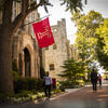 Students walking across Polett Walk on a sunny clear day. The cherry Temple T flag waves above them.