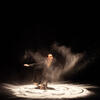 A dancer performs on stage, swirling in sand, creating a unique visual effect.