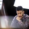 A Music Theory student, with hand on chin, looks down at his work while sitting among other students.