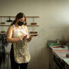 A student wearing a mask and gloves holds a square printing plate in an art studio.