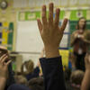 An image of students raising their hand in class