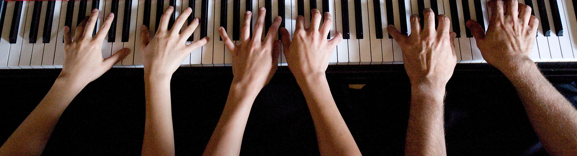 Three pairs of hands playing the piano