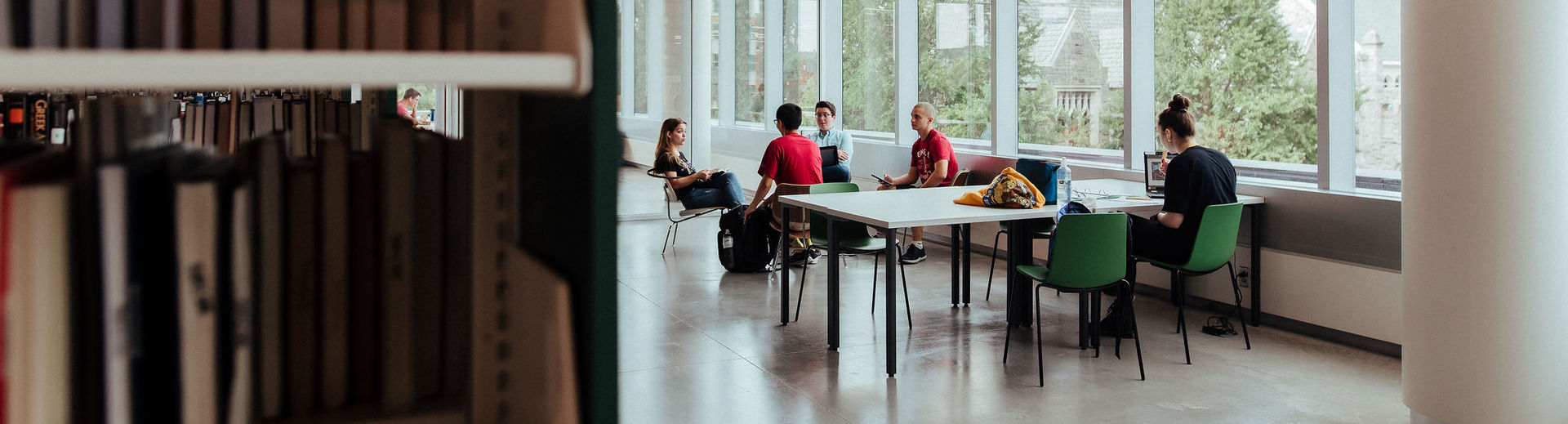 Students are studying at tables in Charles Library, seated by large windows that overlook Main Campus.