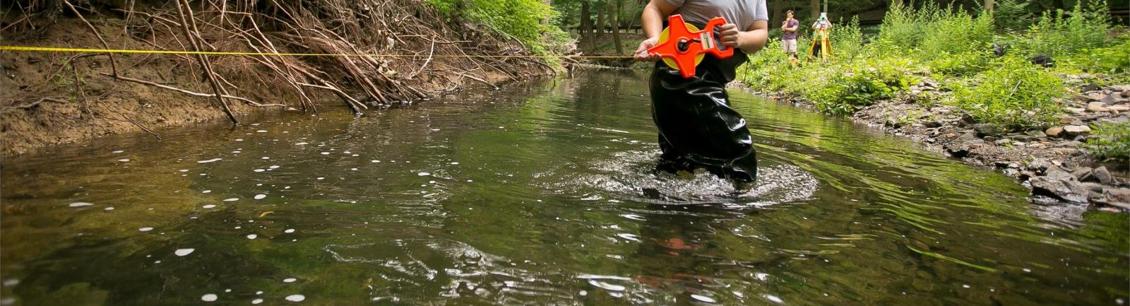 Temple environmental studies student standing in a creek in the woods performing an experiment.