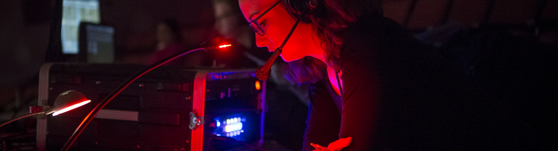 A woman with a headset reads in a darkened room backstage.