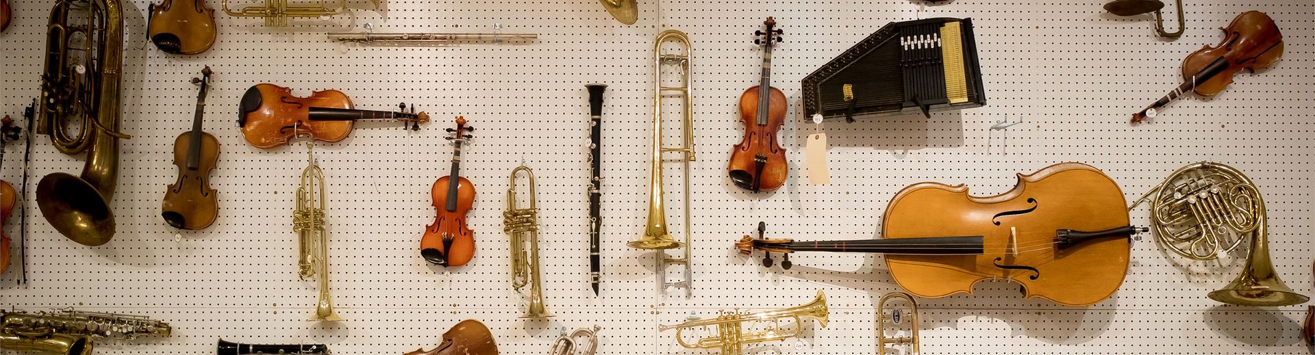 Many different instruments hanging on a pegboard wall.