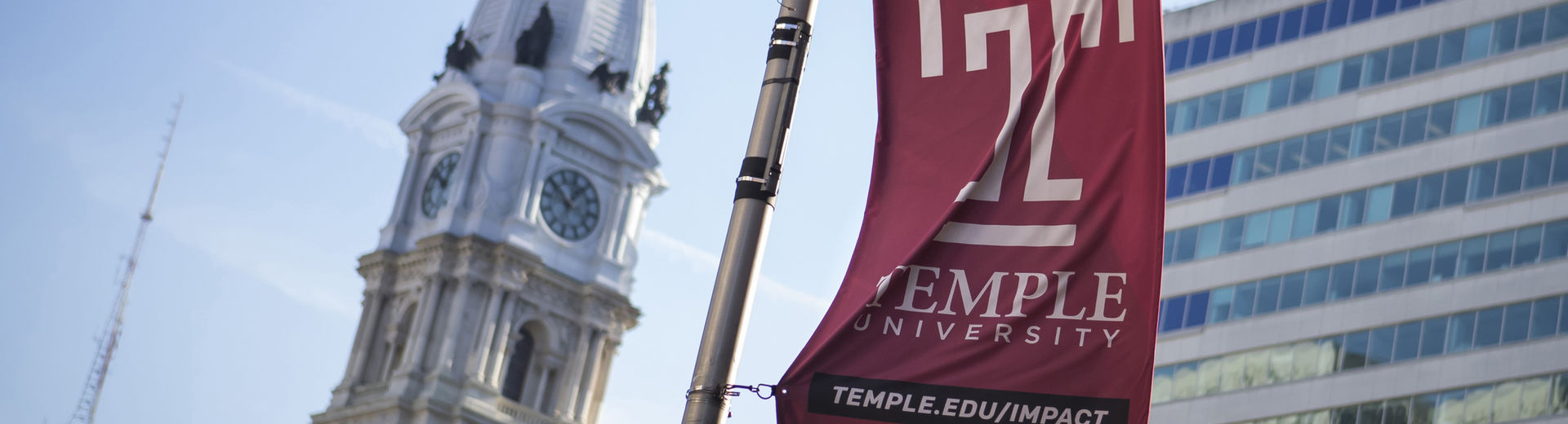 The Temple cherry T flag waves in front of the Philadelphia City Hall building