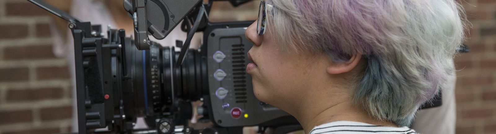 A student filming with two students looking on from the other side.