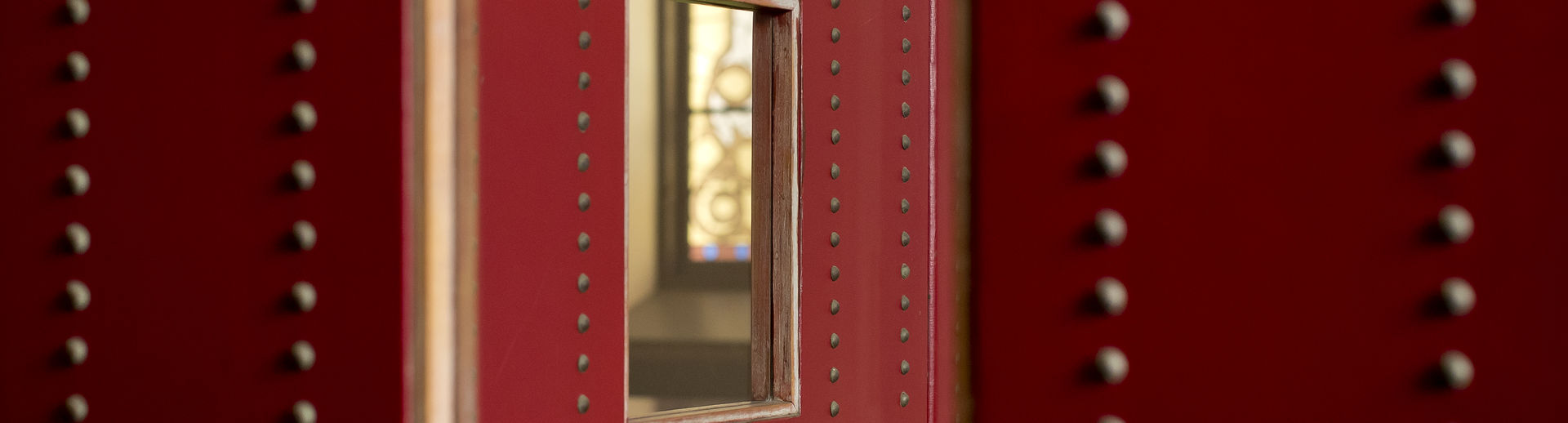 A close up of a mirror within a red frame and a wall laden with studs.