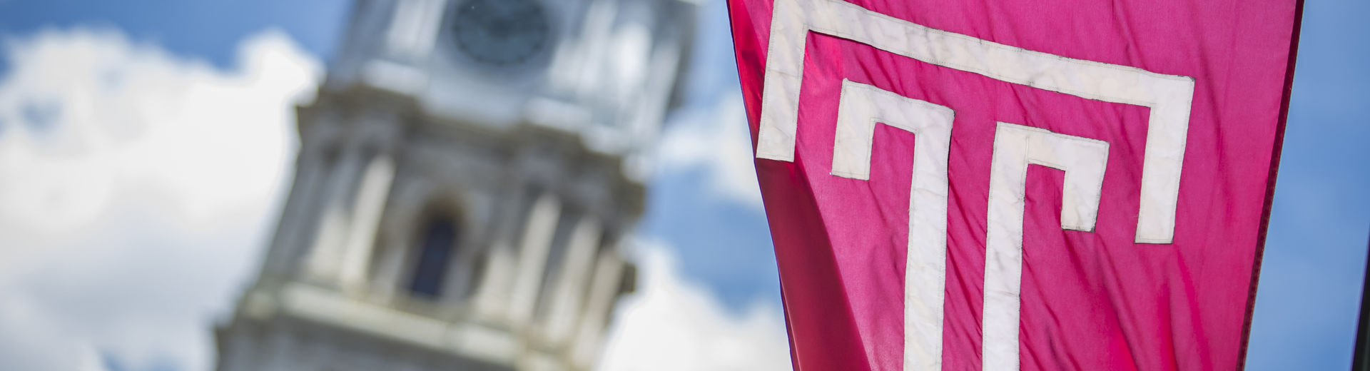 The cherry red Temple T flag waving in front of Philadelphia City Hall on a sunny day.