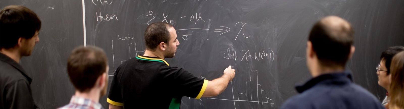 Mathematics professor writing on a chalkboard with students gathered around