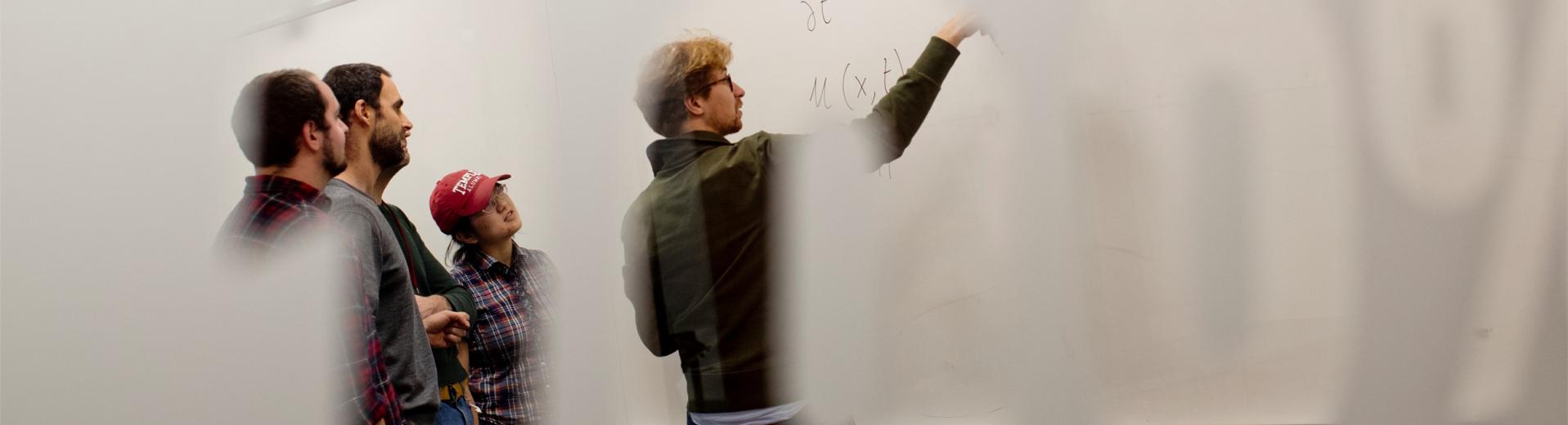 Students pointing to a math equation on a white board in a College of Science and Technology classroom.