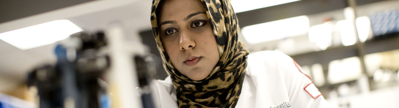 A student wears a white coat while working in a lab.