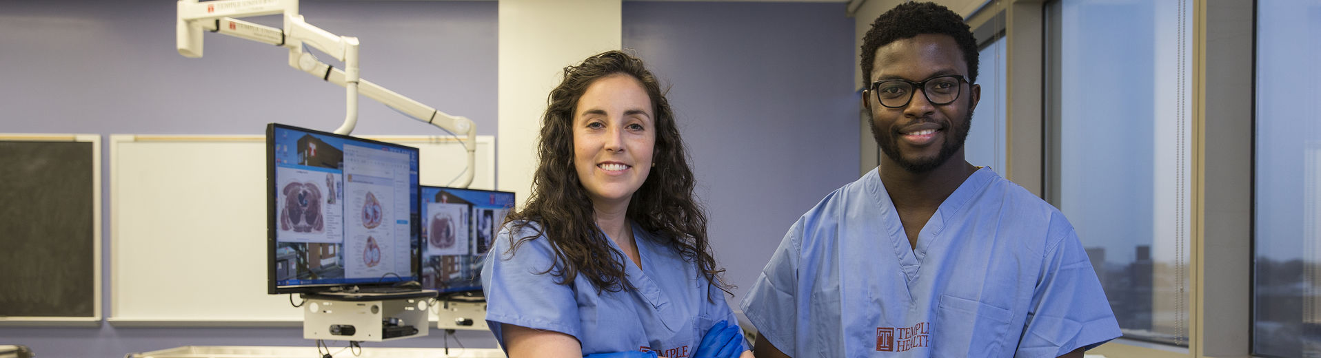 Two MD students wearing scrubs and smiling at the camera