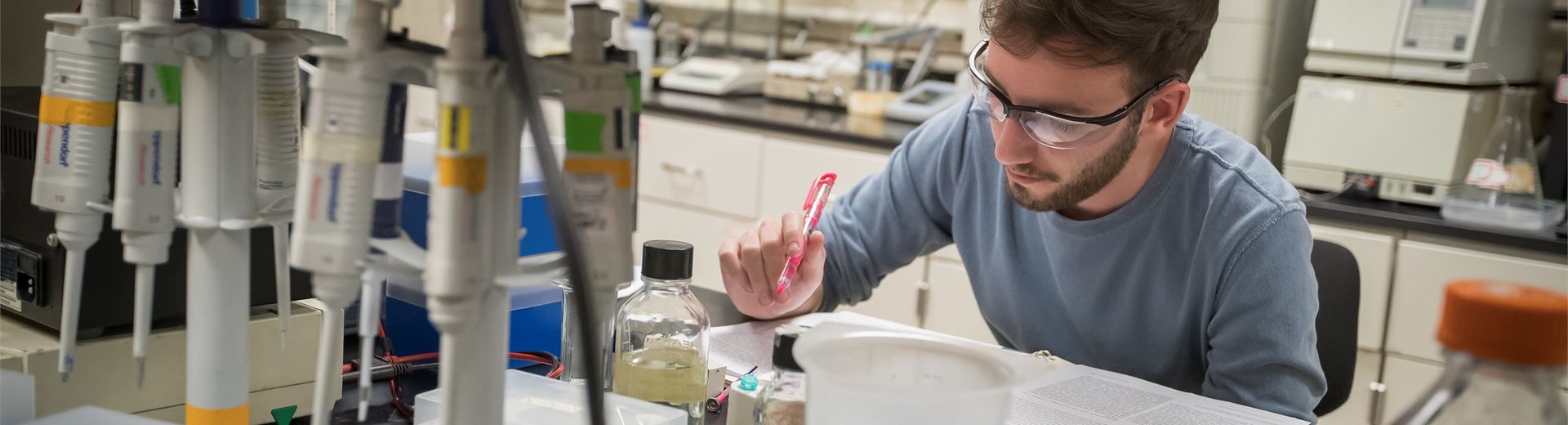 Temple student sitting over book, highlighter in hand, in a College of Science and Technology laboratory.