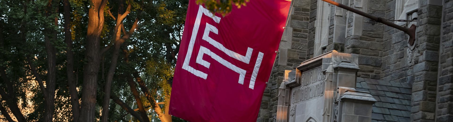 The cherry red Temple T flag hanging outside of Sullivan Hall on Main Campus