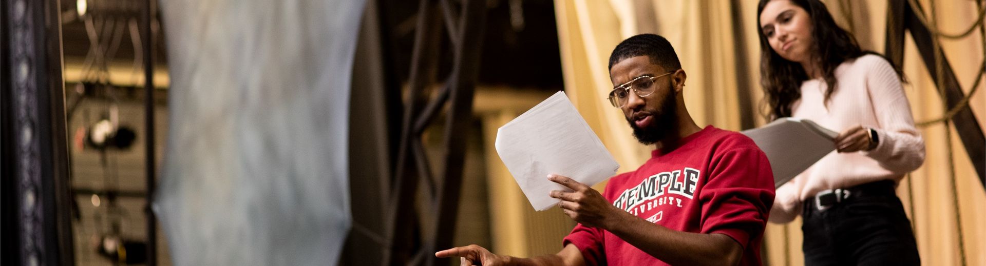 Two actors stand on stage and look at their scripts.