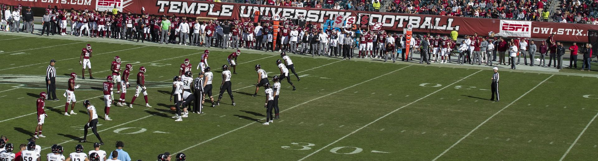 Temple University football players play a game while fans watch from the stands