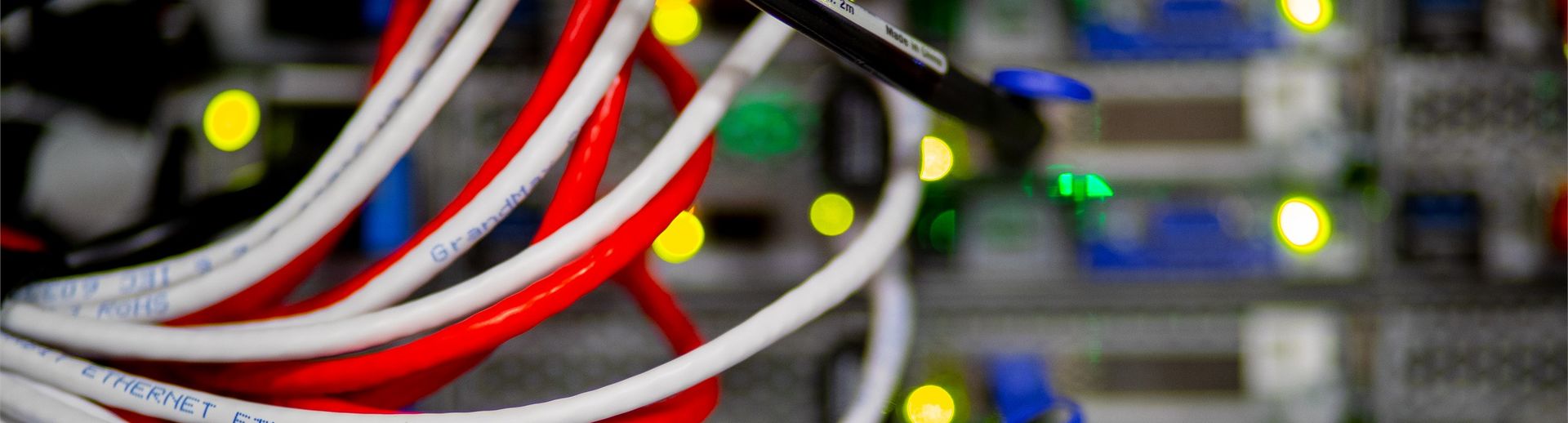 Red and white strands of computer cable fanning out from the back of a stack of servers.