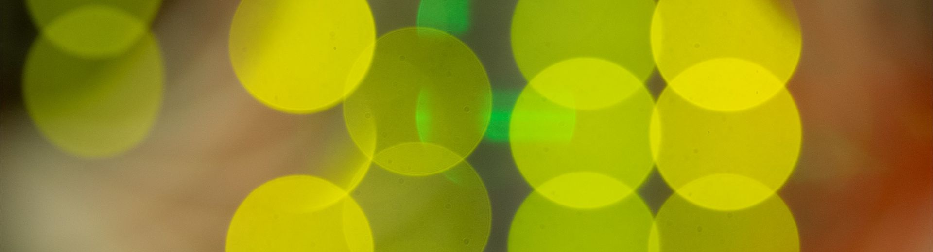 Image is a super close up shot of lights in the back of computer servers resulting in an image of overlapping bright yellow discs of color.