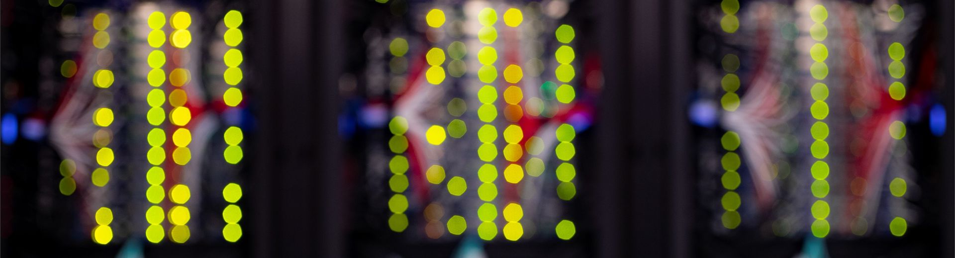 Blurred image of the back of computer servers resulting in a very primary colorscape with columns of bright yellow circles.