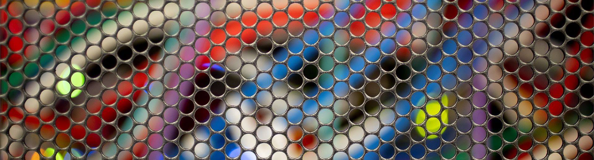 Close up picture of colorful computer cables behind a metal grid of circles.