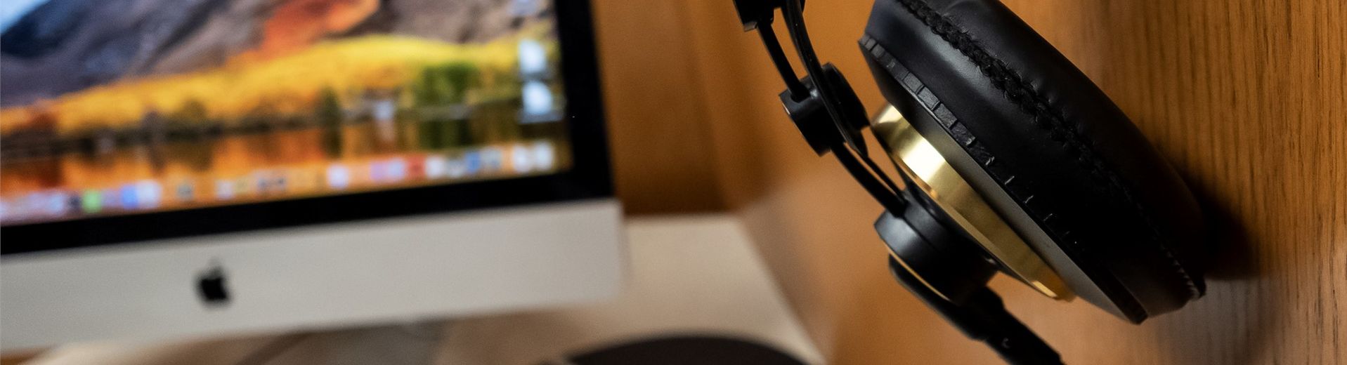 Headphones hanging from a wall next to a Mac computer.