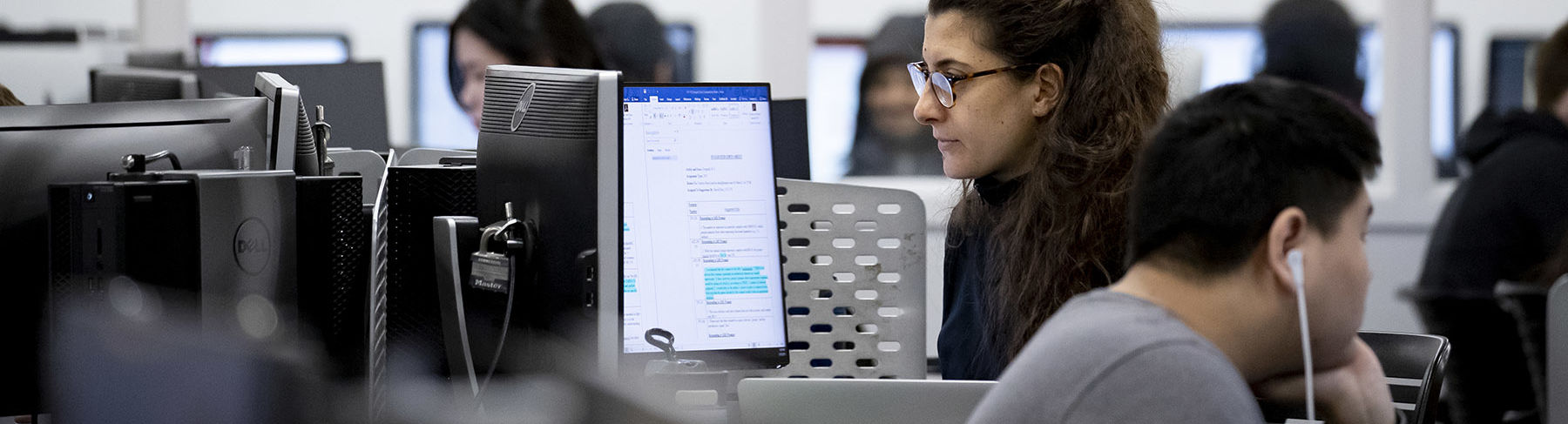 A woman sitting and looking at a computer screen in a technology lab.