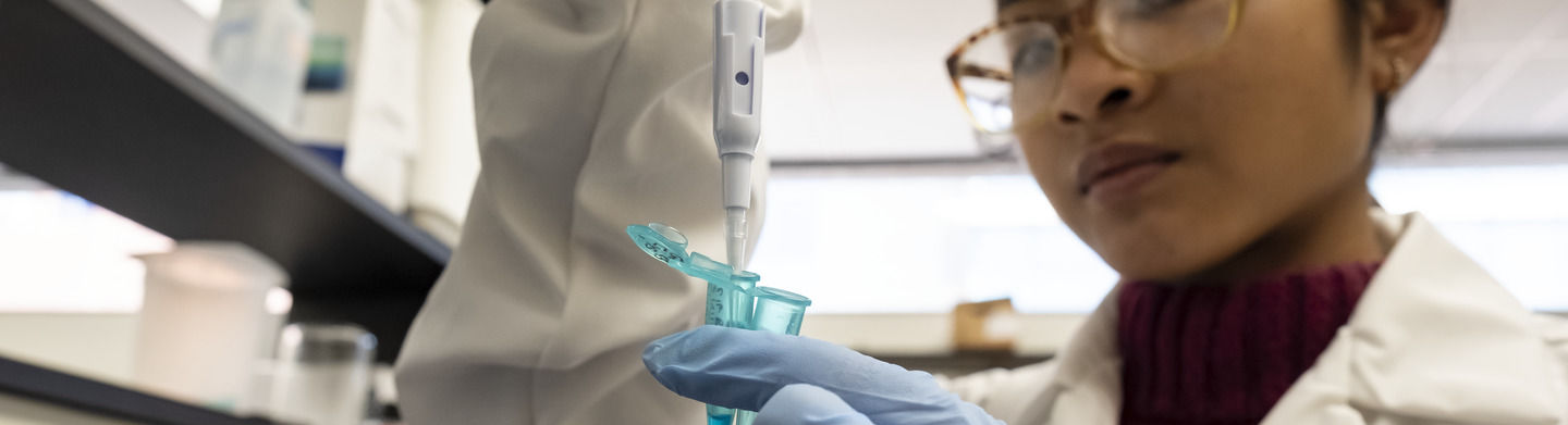 A student wearing gloves injects a liquid into a blue tube while working in a lab.
