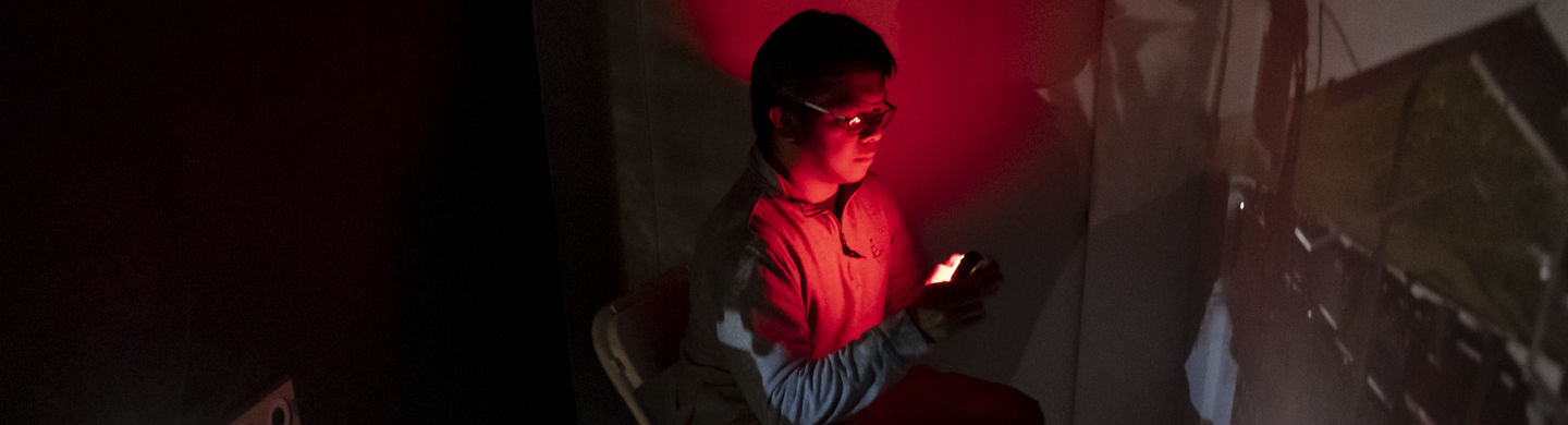 A person sits on a chair in a dark room with red light over their head and chest.