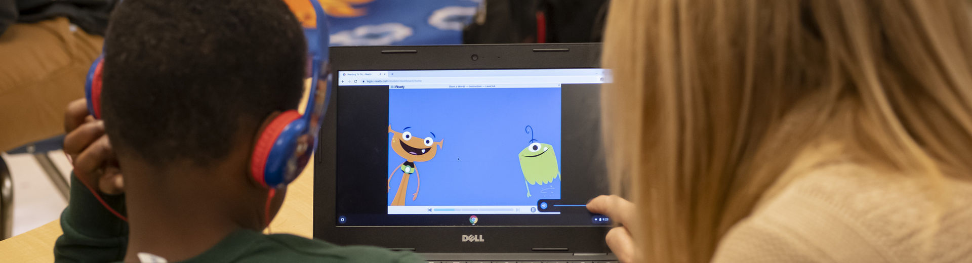 teacher and young student watching a children's program on a laptop.