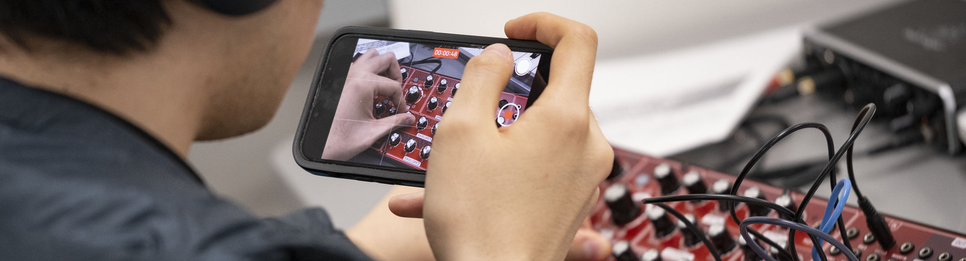 A student records a video while adjusting the dials on a synthesizer.