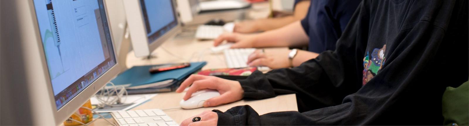 Girl with glasses sitting in front of a computer screen with hands on keyboard in a lab at Temple.