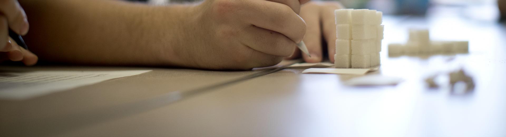 Student writing in a classroom with stack of sugar cubes