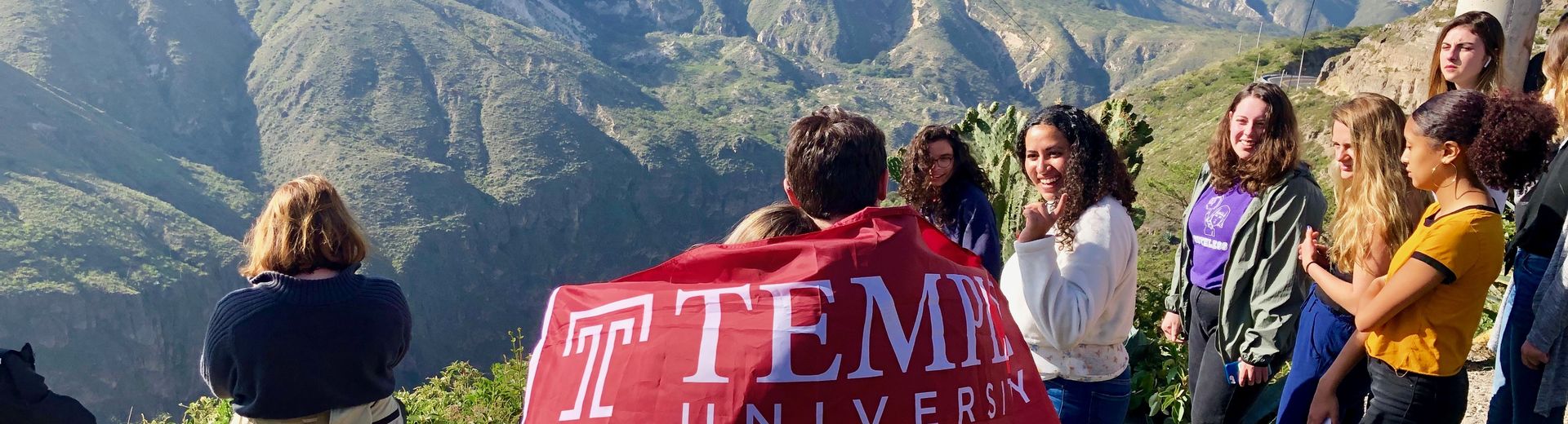 Students on top of a mountain carrying a cherry red Temple flag