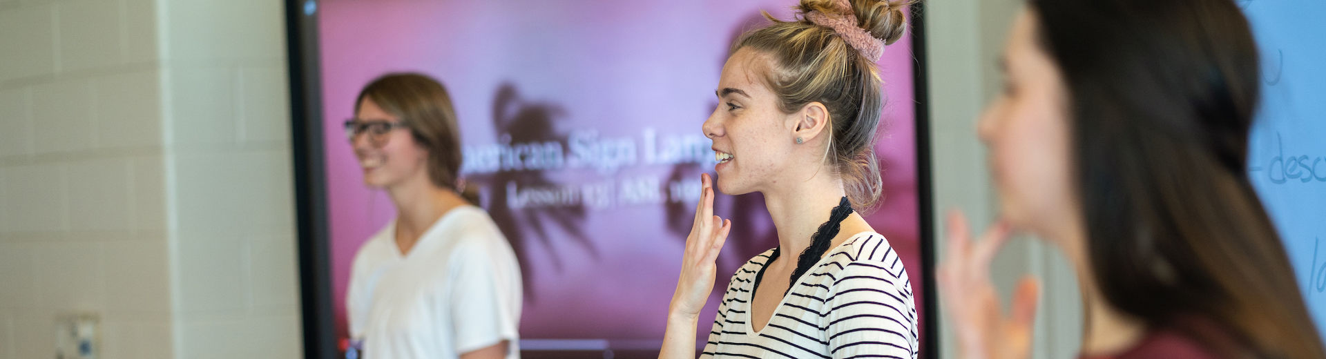 Three students are shown with an American Sign Language sign in the background.